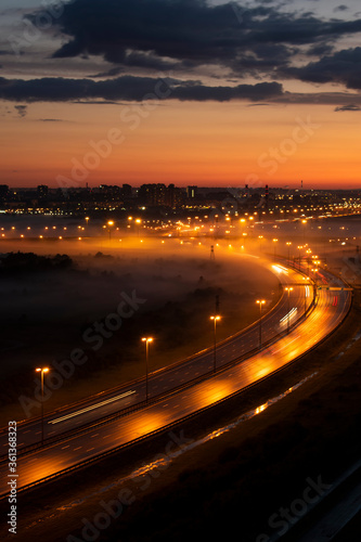 Night highway in the fog. Bright light from the headlights stretches along the road from a long exposure. © Anastasiya