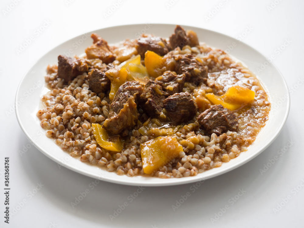 Hungarian goulash. Buckwheat with beef. White round plate on a white background Hungarian goulash. Buckwheat with beef. White round plate on a white background