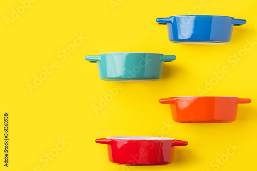 Bild auf Leinwand Set of multicolored ceramic cooking pots tureens cocottes on bright yellow background