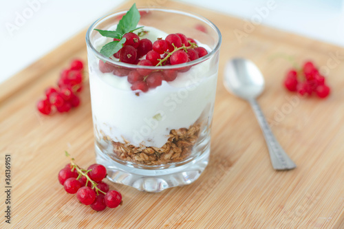 Light summer breakfast parfait with granola, vegan greek yogurt, redcurrant berries and garnished with basil leaves. Light and airy aesthetic