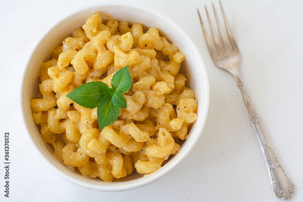 Simple American stove-top elbow macaroni and cheese also called mac n cheese garnished with basil on white background