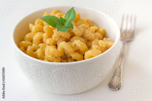 Simple American stove-top elbow macaroni and cheese also called mac n cheese garnished with basil on white background
