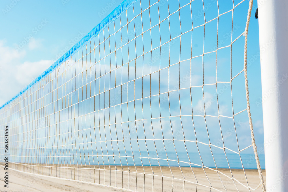 Close up of volleyball net at empty beach by ocean seaside. Blue sky sea white sand background. Summer sports recreation leisure activities concept