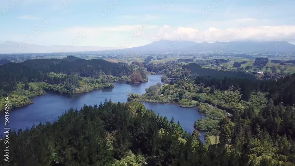 Aerial shot, flying over forest into the lake with Mount Taranaki at the back in New Plymouth New Zealand. Aerial shot, flying over forest into the lake with Mount Taranaki at the back in New Plymouth New Zealand.