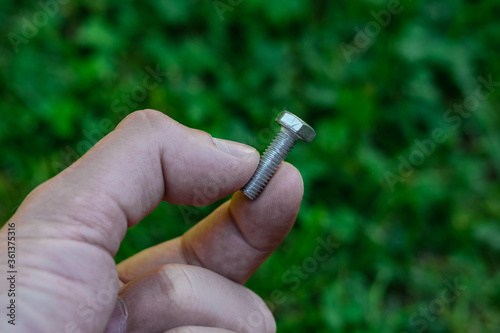 A young man holds one bolt with two fingers on a background of green grass.