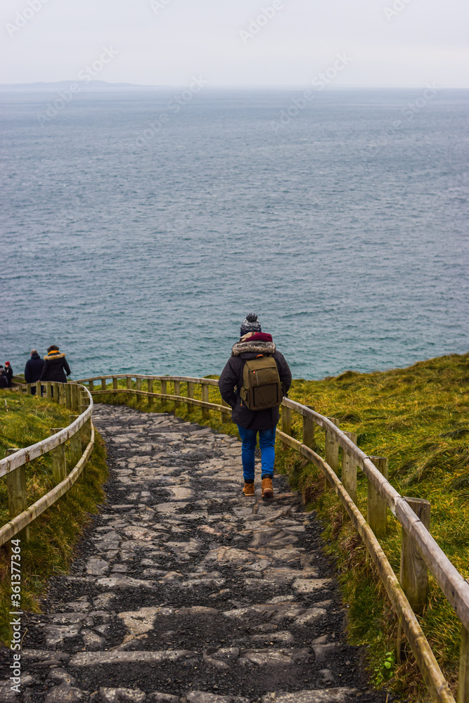 Photo of a young and attractive man with beard standing in the nature with winter clothes and a backpack in the Giants Causeway, Belfast. Holidays concept