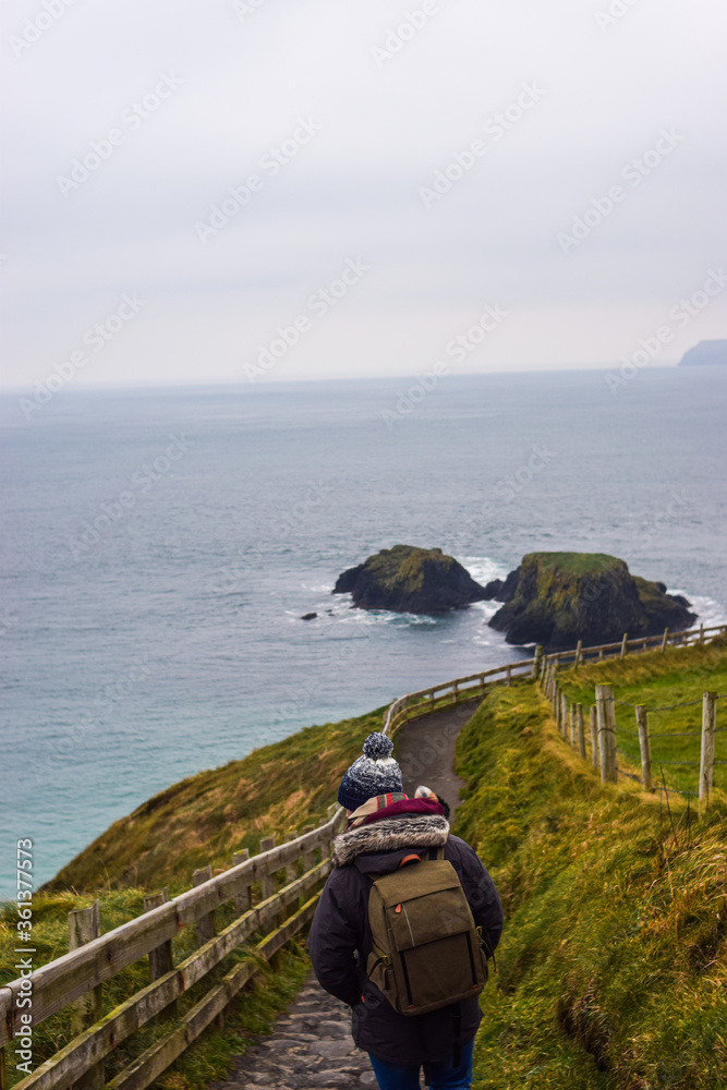 Photo of a young and attractive man with beard standing in the nature with winter clothes and a backpack in the Giants Causeway, Belfast. Holidays concept