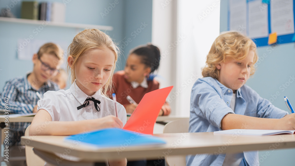 Obraz premium Elementary Classroom of Diverse Bright Children Listening Attentively to their Teacher Giving Lesson. Brilliant Kids in School Writing in Exercise Notebooks, Taking a Test. 