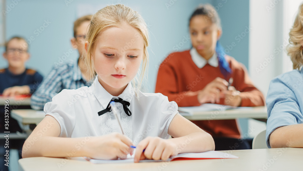 Fototapeta premium In Elementary School Class: Portrait of a Brilliant and Cute Caucasian Girl Writes in Exercise Notebook. Junior Classroom with Diverse Group of Children Working Diligently and Learning New Stuff