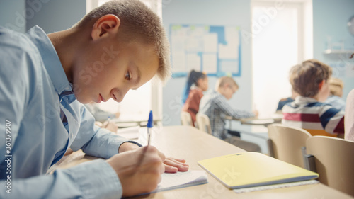 Shot of a Young Boy in School Writing in Exercise Notebooks, Taking a Test. Elementary Classroom of Diverse Bright Children Writing in Notebooks.
