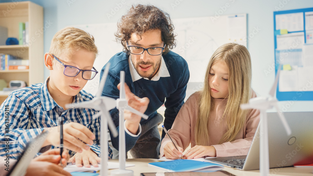 Obraz premium Elementary School Classroom: Enthusiastic Teacher Holding Tablet Computer Explains Lesson to Brilliant Young Children. Kids Learning Programming Languages, Internet Safety and Information Technology