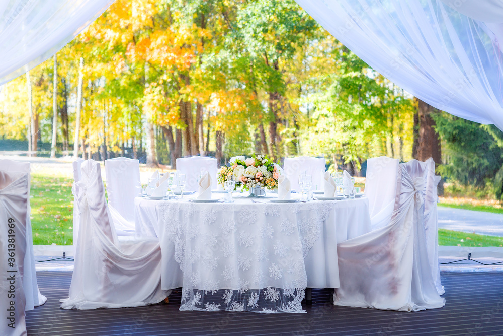 Wedding table with white tablecloth, outdoor setting, view of autumn bright yellow and orange trees