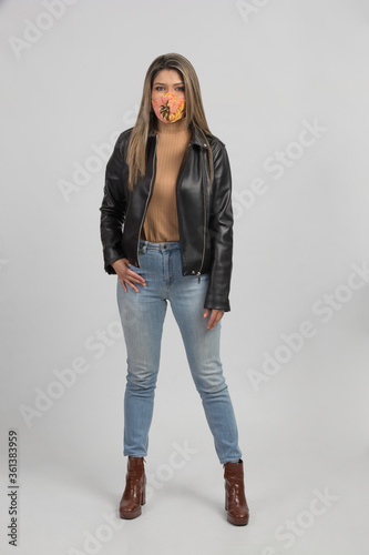 latin woman with colorful mask and leather jacket, standing front, studio photo with gray background photo