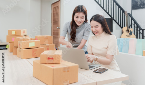 Two beautiful Asian women are checking orders by laptops via the internet. And pack the paper box With a happy smiling face, being a new normal online business