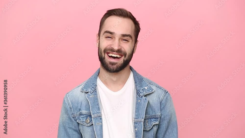 Handsome bearded young man guy 20s years old in denim jacket white t-shirt isolated on pastel pink background studio. People sincere emotions lifestyle concept. Looking at camera with charming smile Handsome bearded young man guy 20s years old in denim jacket white t-shirt isolated on pastel pink background studio. People sincere emotions lifestyle concept. Looking at camera with charming smile