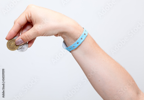 Female hand with blue hotel bracelet gives tip with coins money, grey background photo