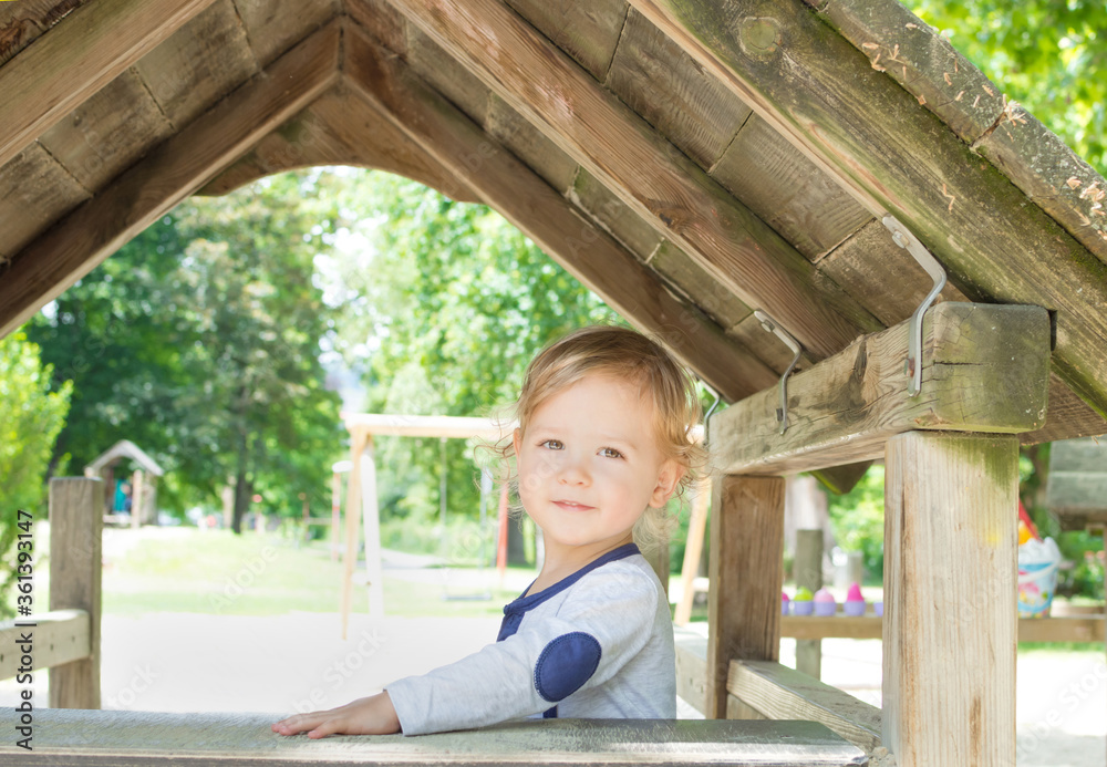 Obraz premium Cute little child having fun inside a wooden house in the park. Beautiful summer sunny day in children playground