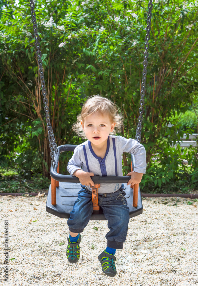 Cute little child having fun on a swing in the park. Beautiful summer sunny day in children playground Cute little child having fun on a swing in the park. Beautiful summer sunny day in children playground
