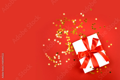 Minimalist Christmas composition with gift box  golden confetti on red background. Greeting concept for New Year  Valentines day  Womens day or birthday.  Top view.  Copyspace.