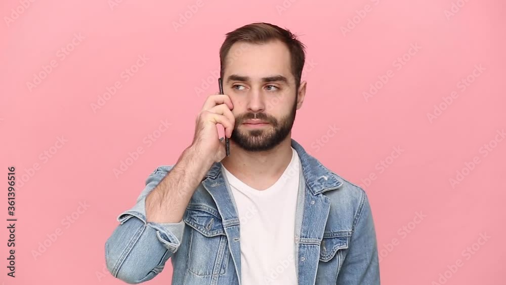 Disgusted fun young man guy 20s years old in denim jacket white t-shirt hold do not want talking to girlfriend using mobile phone isolated on pastel pink background studio. People lifestyle concept Disgusted fun young man guy 20s years old in denim jacket white t-shirt hold do not want talking to girlfriend using mobile phone isolated on pastel pink background studio. People lifestyle concept