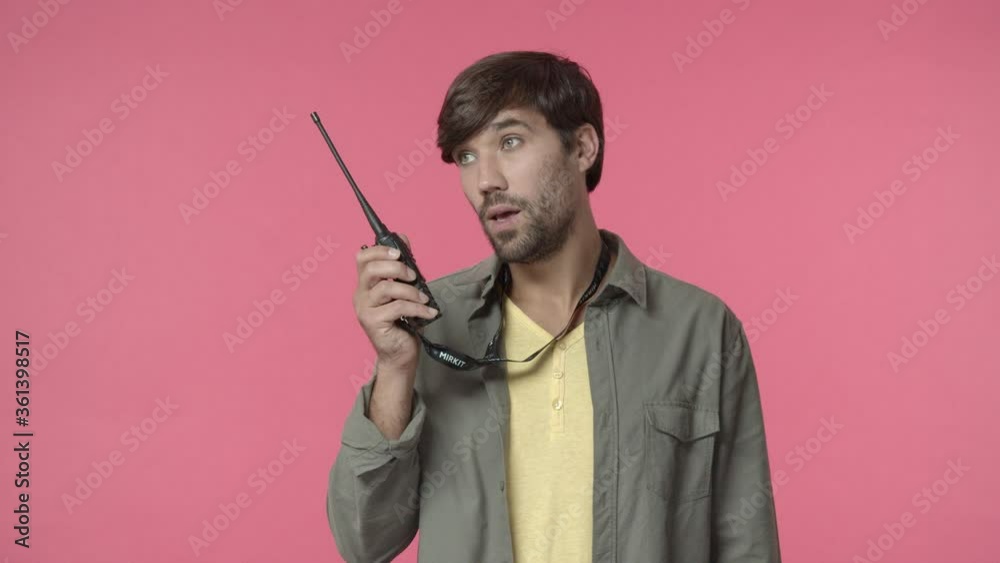 Handsome young store clerk standing over counter, reply to coworker over portable radio set with annoyed, tired of dumb questions face, saying yes, contact colleague over transmitter