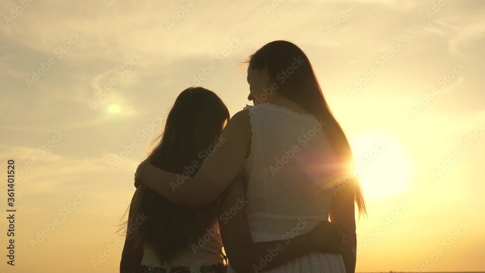Happy family mom and daughter in field at sunset. Mom hugs daughter, they admire beautiful sunset. concept of happy family of children and children. mother and baby walk in park, field, in sun