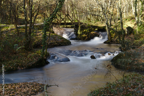 Mountain river streams with wood and stone bridge in Galicia forest, long exposure