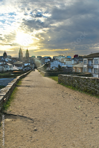 Roman wall of Lugo, a world heritage site, with the towers of the cathedral in the background and the city at dawn with the sun backlit