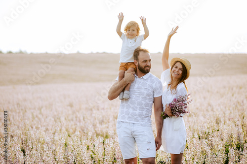 Happy family portrait outdoor at the sunset time. People having fun on the field. Concept of friendly family and of summer vacation. Parents and son spending good time. White dress. Straw hat.