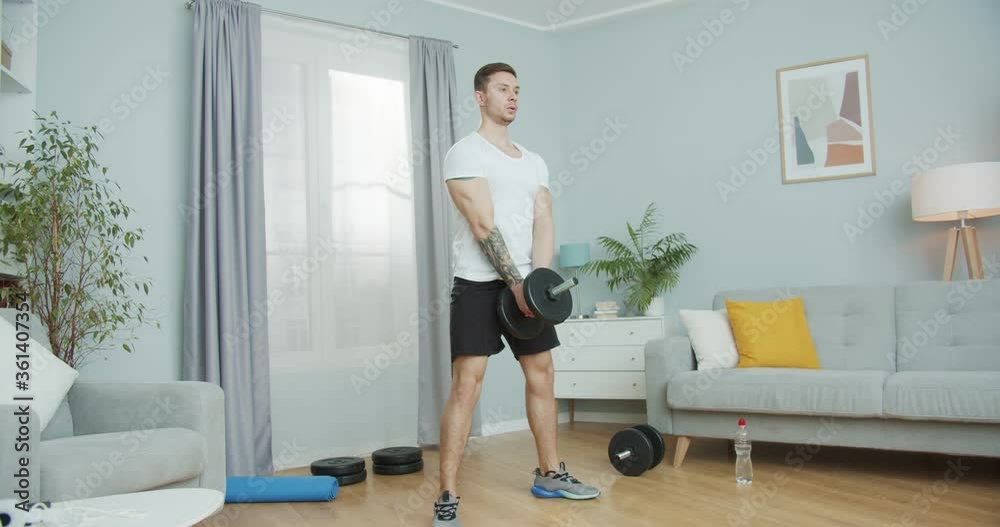 Sporty caucasian guy working out at home during pandemic. Athletic fit male doing squat exercises with a dumbbell to strengthen muscles, tone up, fit. Indoors training. Self-isolation, health concept. Sporty caucasian guy working out at home during pandemic. Athletic fit male doing squat exercises with a dumbbell to strengthen muscles, tone up, fit. Indoors training. Self-isolation, health concept.