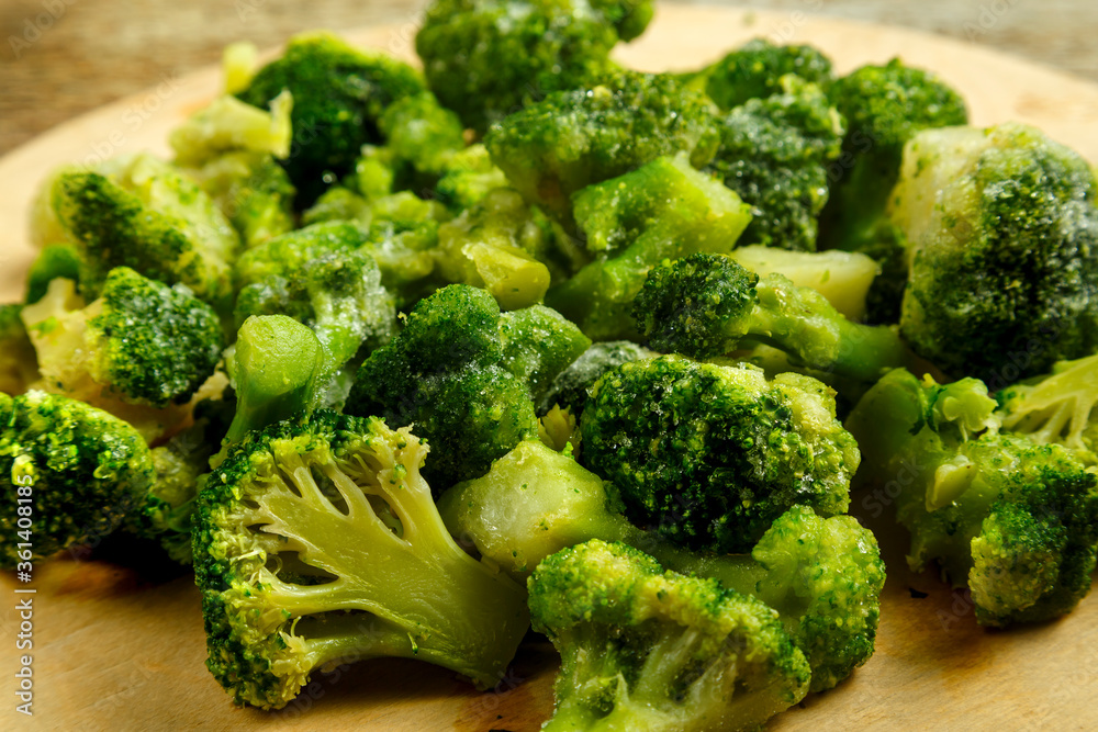 Scattered frozen broccoli on a round wooden board. Scattered frozen broccoli on a round wooden board.