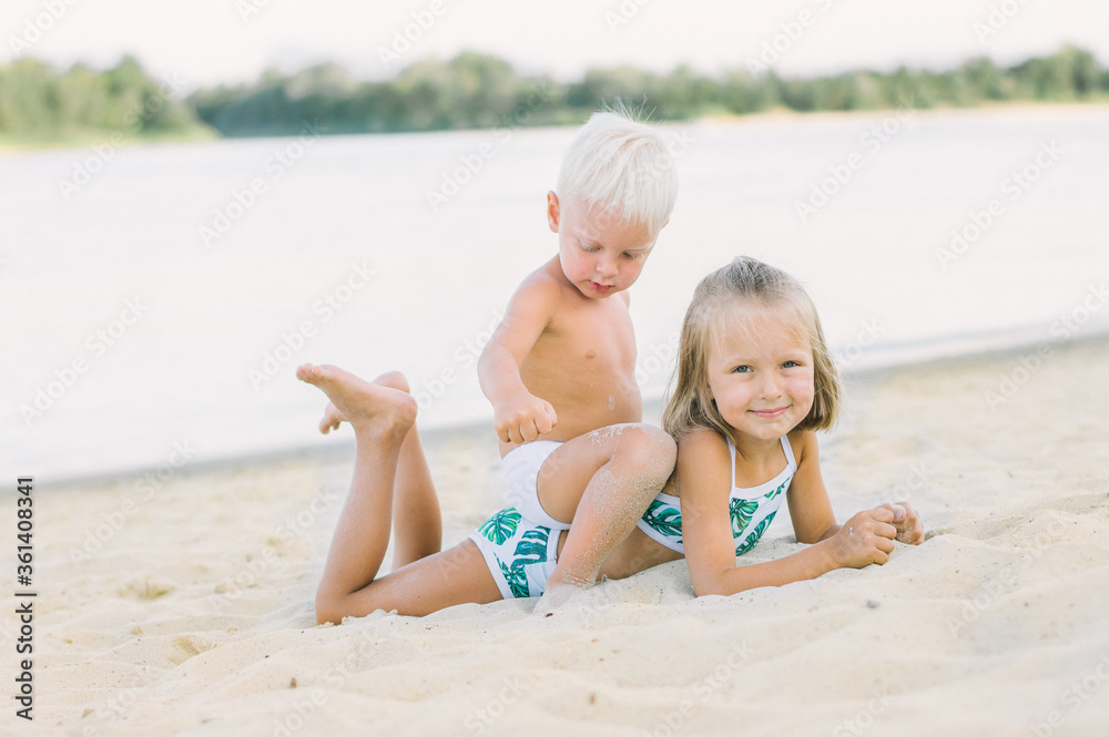 A boy sits on a girl on the beach. Brother and sister play. Sea, summer, beach.