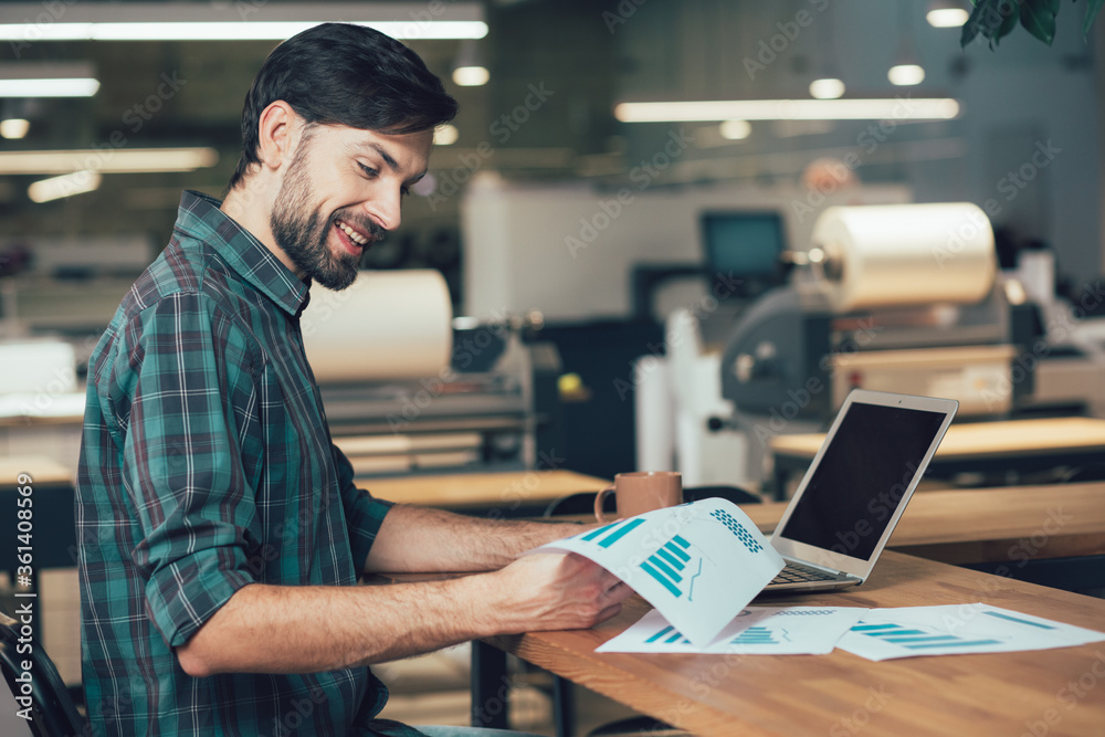 Mirthful entrepreneur with graphics on paper and modern gadget