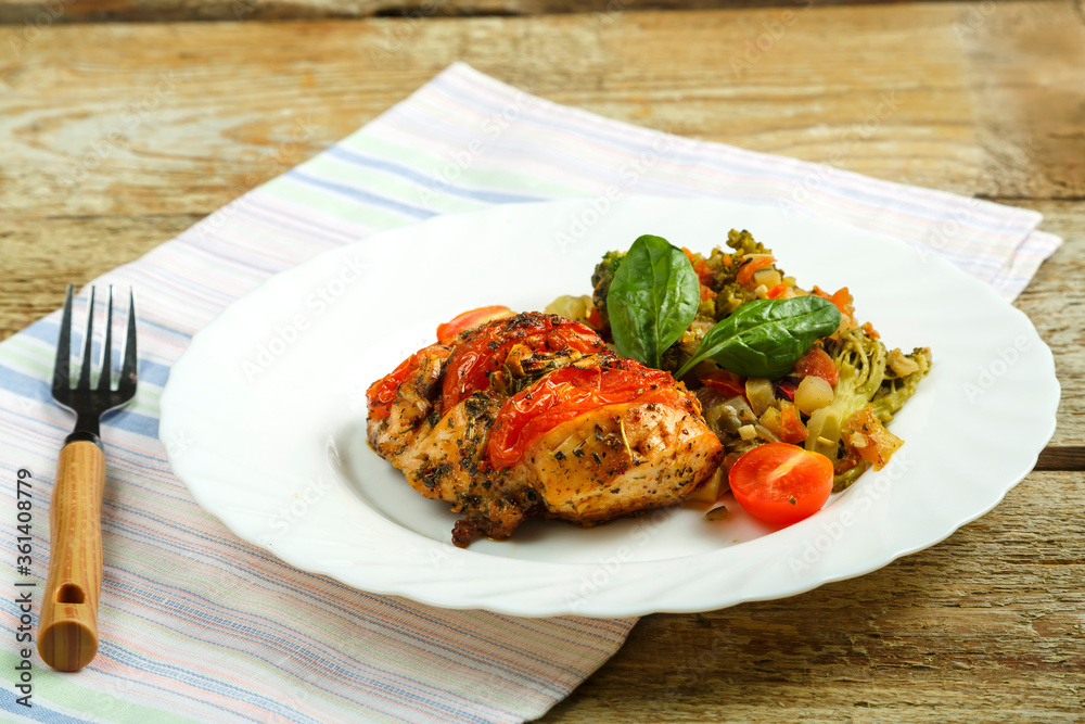 Baked chicken breast in spices with tomatoes with a side dish of vegetables on a white plate with a fork on a napkin. Baked chicken breast in spices with tomatoes with a side dish of vegetables on a white plate with a fork on a napkin.