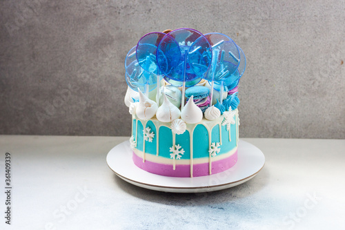 Blue winter cake with white chocolate, lollipops and fondant snowflakes. Grey background.