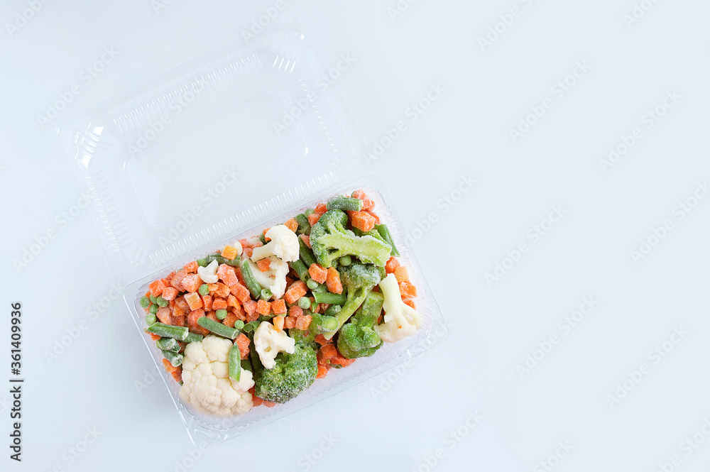 Frozen vegetable mix in transparent plastic container on a white background.