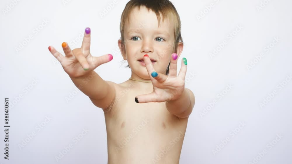 A cute little boy stands with arms extended forward showing his painted multi-colored fingers against white background A cute little boy stands with arms extended forward showing his painted multi-colored fingers against white background