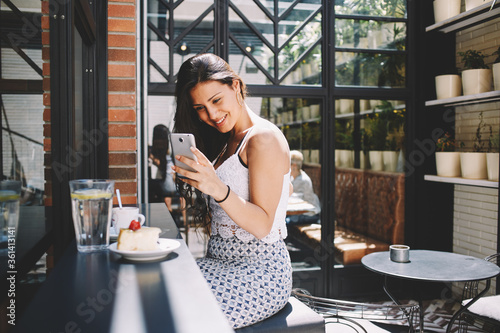 Portrait of smiling gorgeous female taking picture of cappuccino cup and berries cake with her smart phone camera, attractive appearance young woman using her cellphone while photographing breakfast