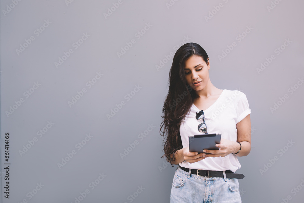 Charming latin woman holding her digital tablet computer while standing against street wall background with copy space area for your text message or information,female using touch pad in urban setting Charming latin woman holding her digital tablet computer while standing against street wall background with copy space area for your text message or information,female using touch pad in urban setting