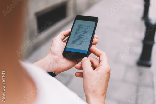 Cropped image of female tourist using mobile phone for navigation while lost way during walking around the city, woman reading text message on cell telephone while strolling outside in urban setting