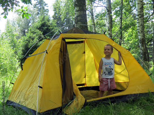 A child plays in a camping yellow tent in nature among the trees © Екатерина Воронина