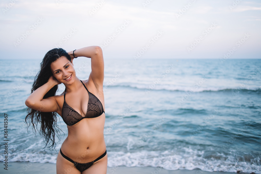 Half length portrait of gorgeous latin woman smiling and feeling so good while enjoying her summer vacation holidays, cute charming girl in sexy bikini standing on the shore with copy space area