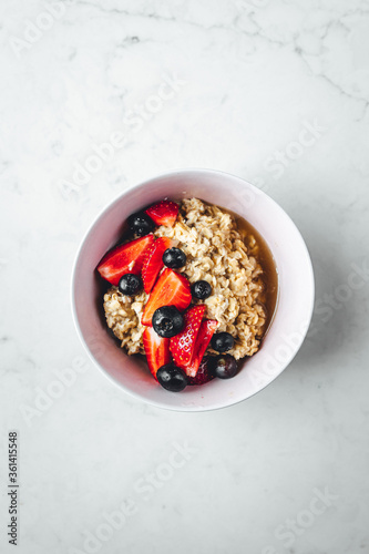 Close up view on oatmeal with strawberries and blueberries on bright textured table