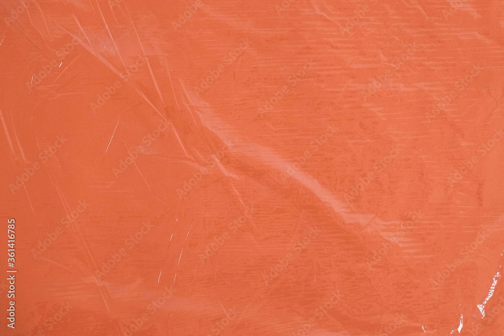 Fototapeta premium Wrinkled transparent plastic texture on an orange background. Transparent cellophane texture on an orange backing. Top view. Copy, empty space for text