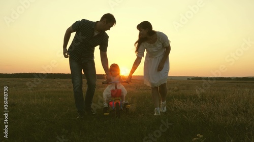 Mom and dad teach a young child to ride a bike at sunset in the park. Teamwork. Silhouette family walk