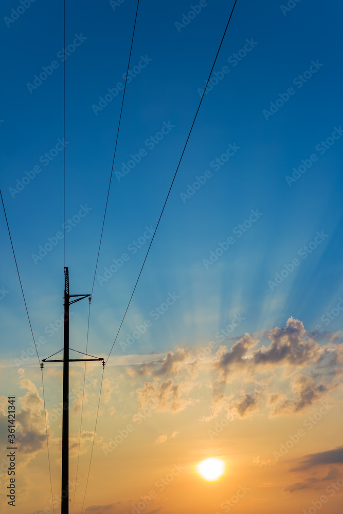 High voltage electricity pylons against beautiful sky with sun rays. Electric pole power lines and clouds.