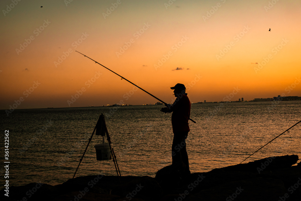 man fishing with fishing rod in sunset, silhouette.