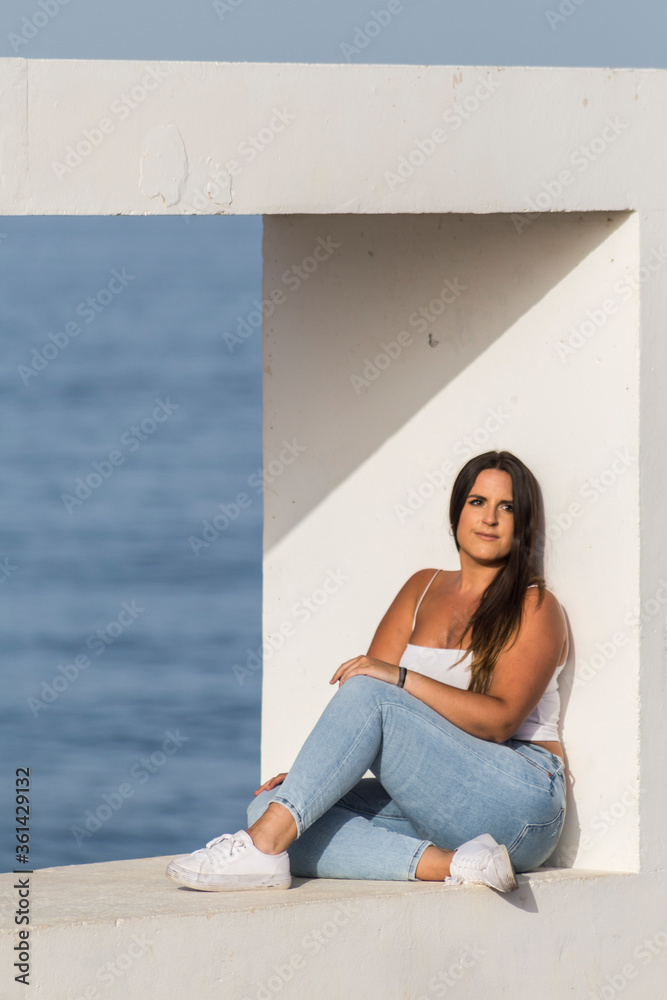 young brunette woman sitting relaxed on a bench overlooking the sea