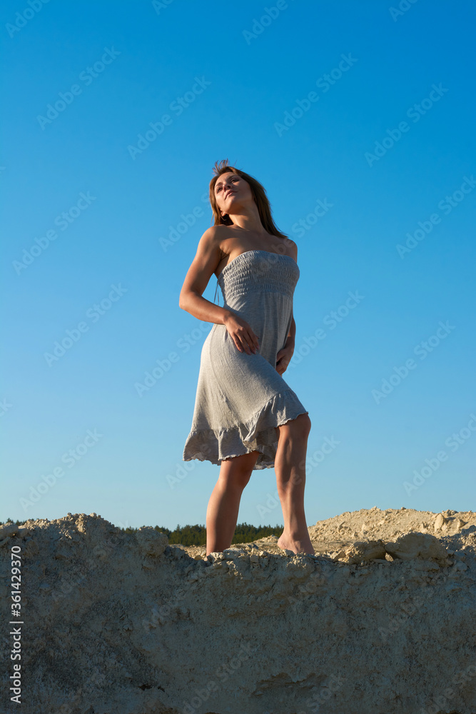 beautiful brunette girl dancing and looking at the sun.girl in a white dress in the desert against the blue sky