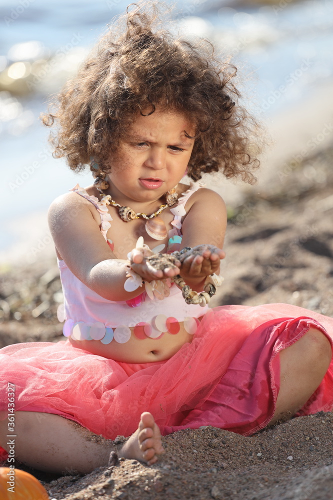 little girl with curly hair on the beach in a pink skirt plays in the ...